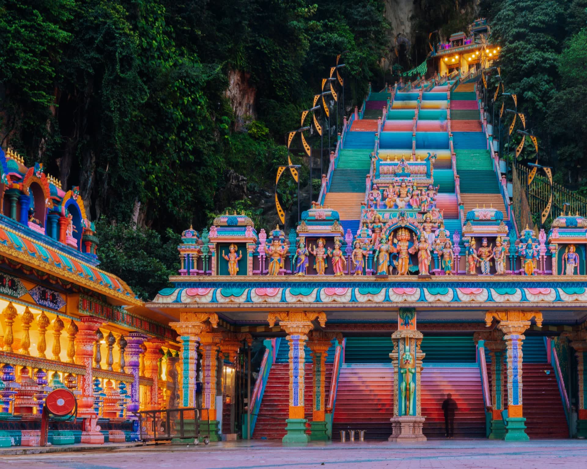 The rainbow-painted stairway at Batu Caves rises from an ornate Hindu temple gateway toward the cave in the limestone cliff.