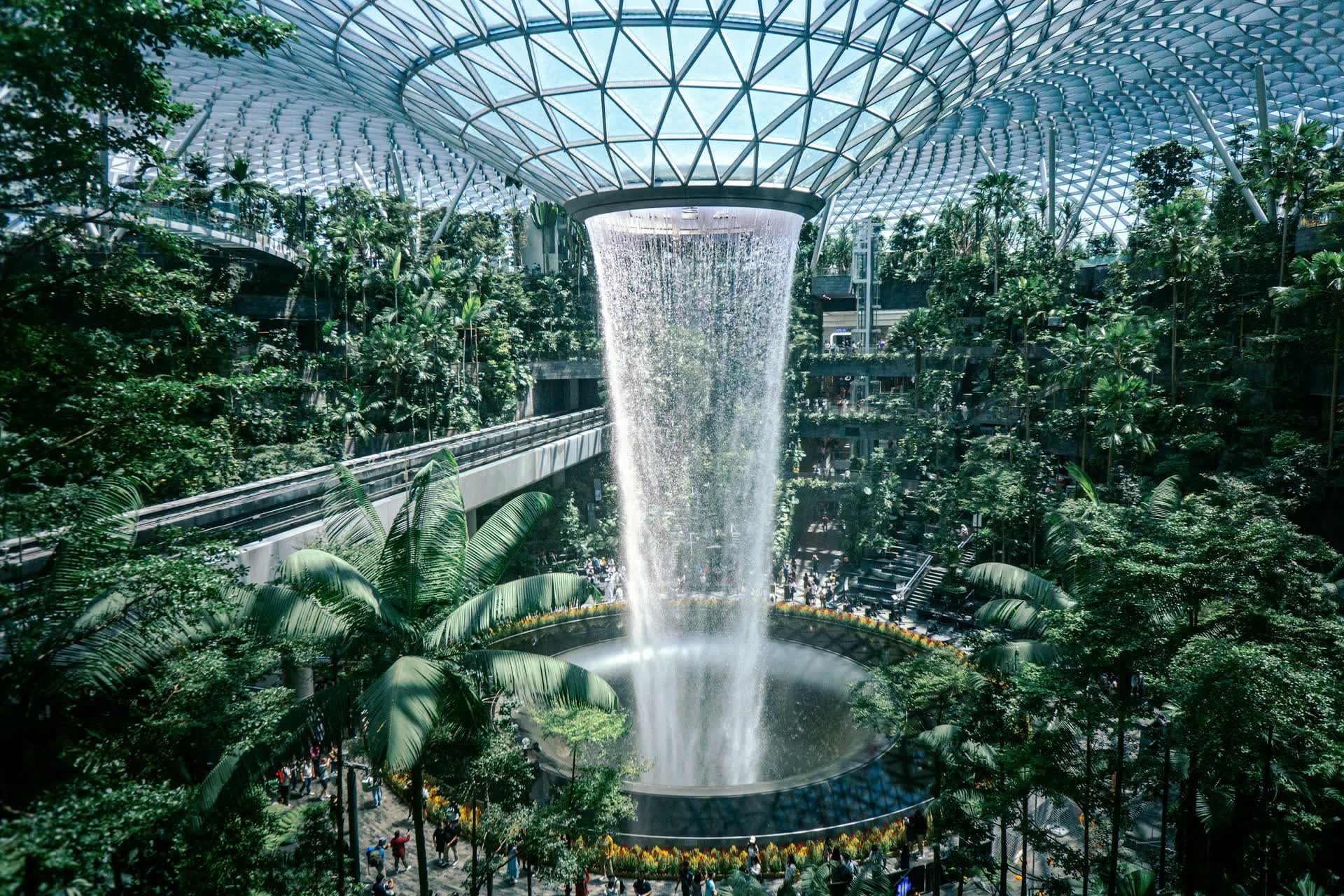 The Rain Vortex waterfall pours through the glass dome of Jewel Changi Airport into an indoor forest.