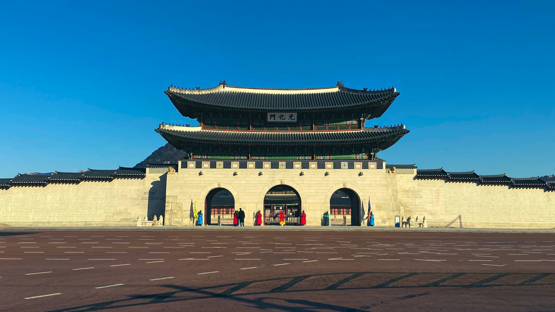 Gwanghwamun, the main gate of Gyeongbokgung Palace in Seoul, with its three arched entrances open beneath a clear blue sky.